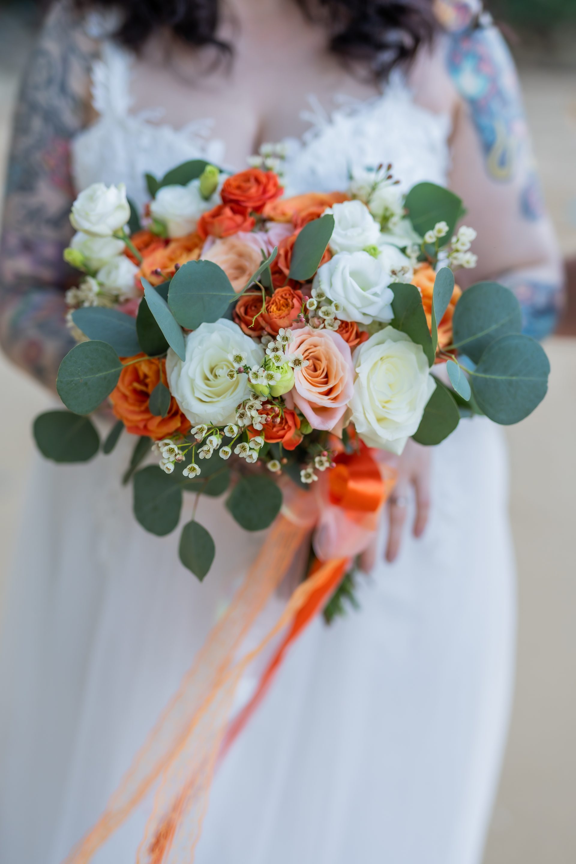 Bride holding a warm-toned orange and white bouquet on a Phuket beach